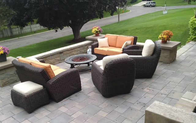 Patio with wicker furniture, a fire pit, and fall flowers. Overlooks a green lawn and road.