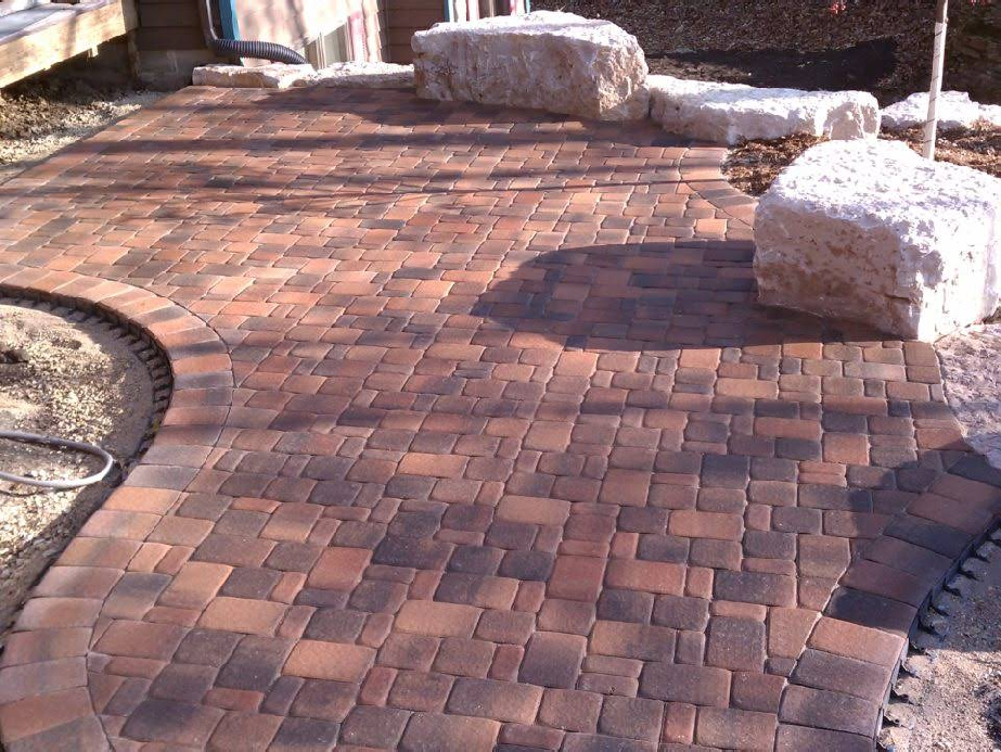 Brick patio with curved edges, two large light-colored rocks, and brown and black bricks.