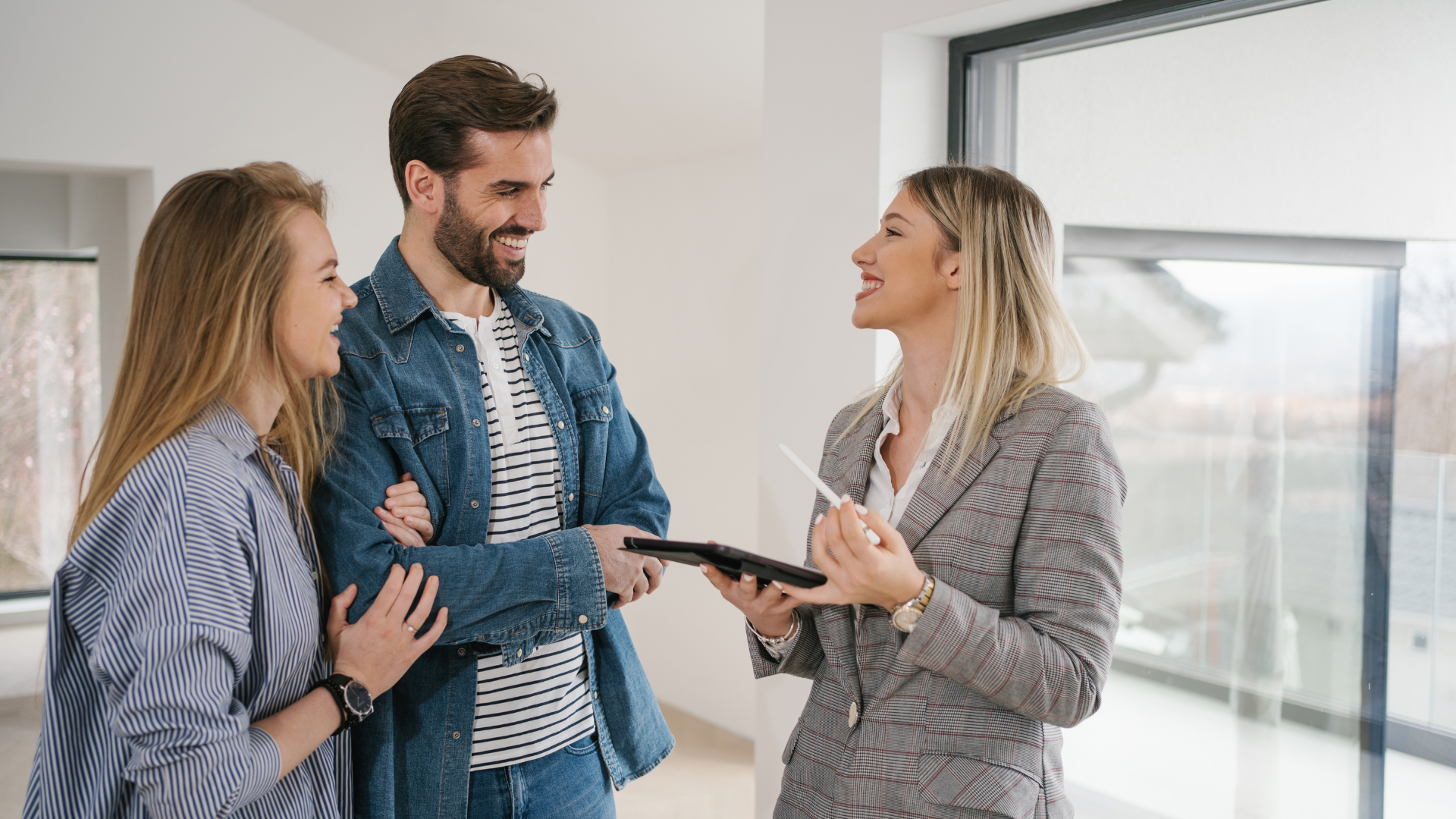 A man and a woman are talking to a real estate agent in an empty apartment.