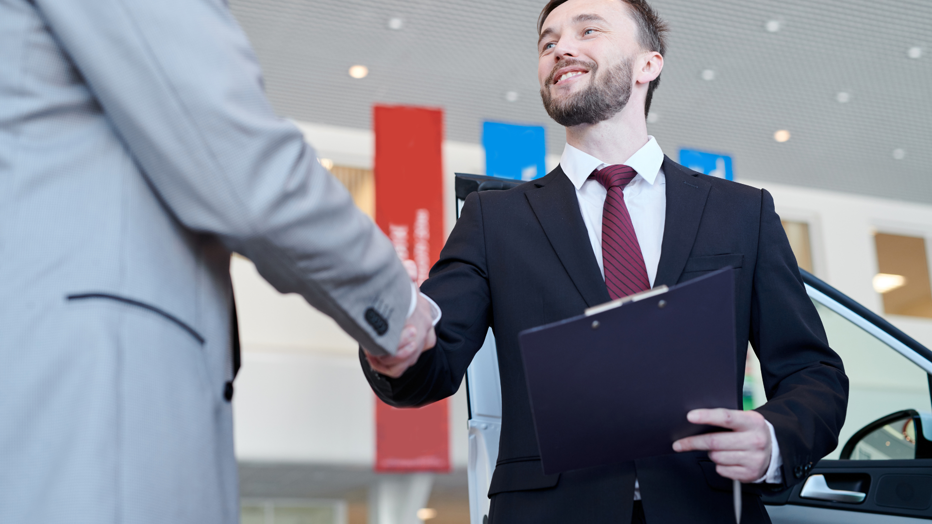 A man in a suit and tie is shaking hands with another man in a car showroom.