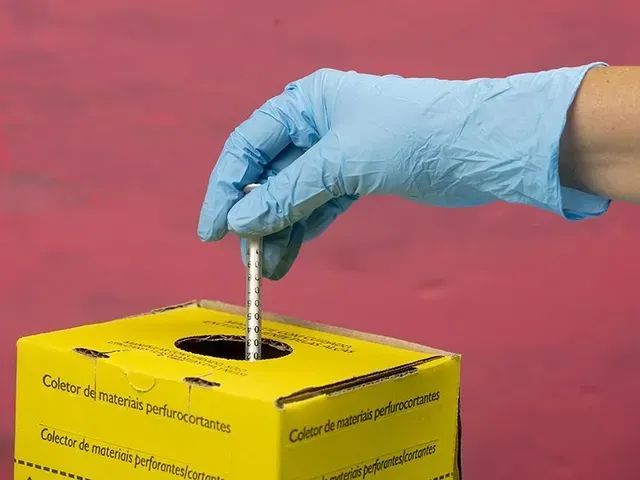 Una mano guantata inserisce una siringa in un contenitore giallo per lo smaltimento di oggetti taglienti.