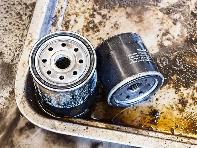 Due filtri dell'olio neri usati sono appoggiati su un vassoio di metallo sporco e macchiato d'olio.