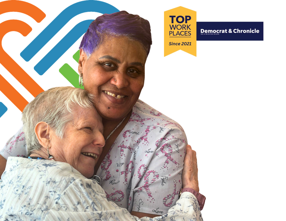a woman is hugging an elderly woman who is sitting in a chair in front of a sign that says top work places 2022