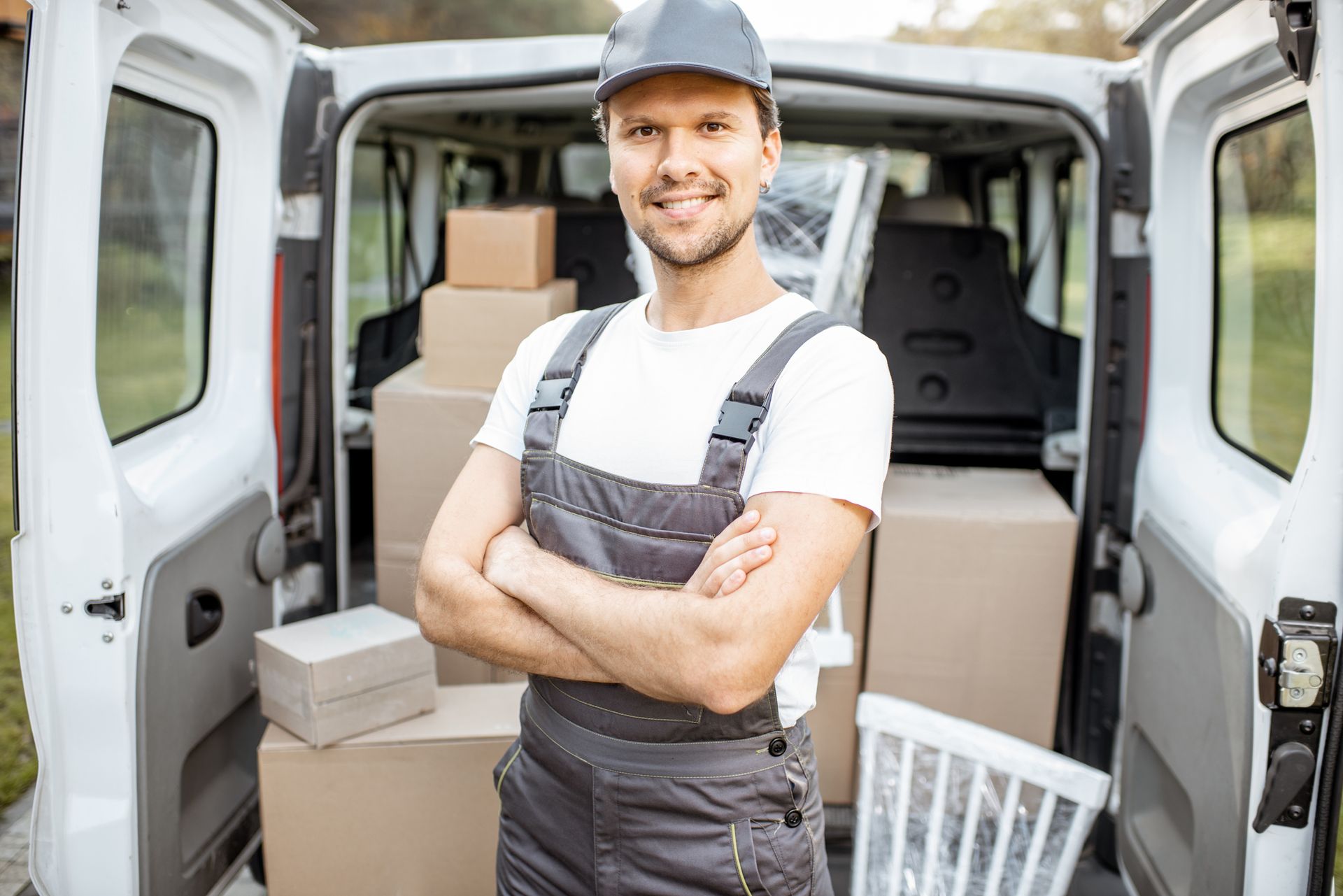 Smiling removalist standing in front of open van loaded with moving boxes and furniture. Smiling removalist standing in front of open van loaded with moving boxes and furniture.