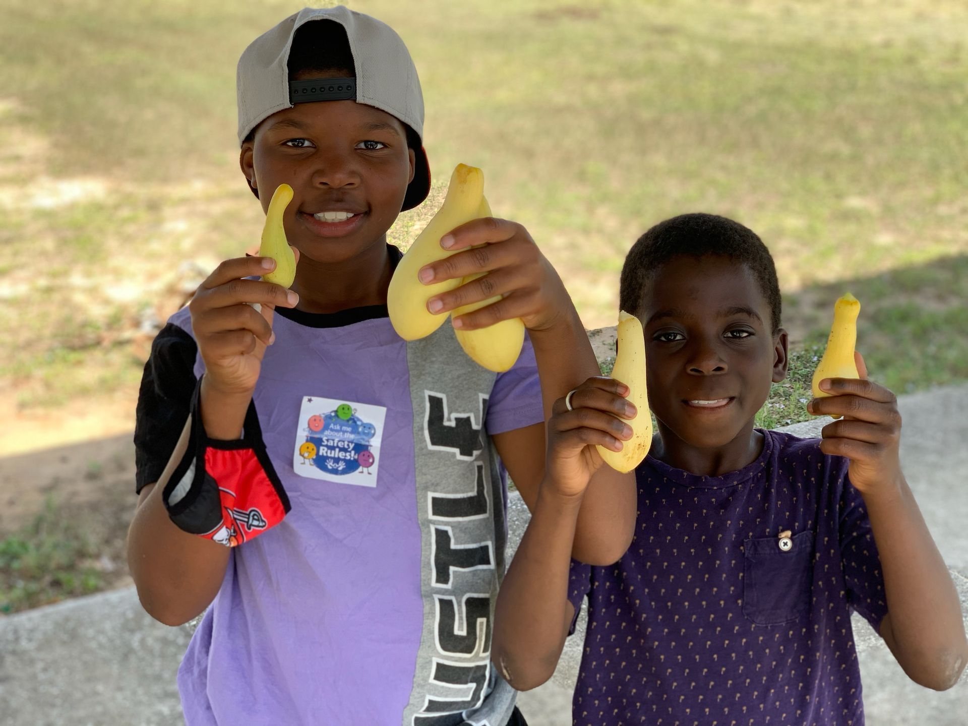 Two children holding banana-shaped popsicles and smiling outdoors