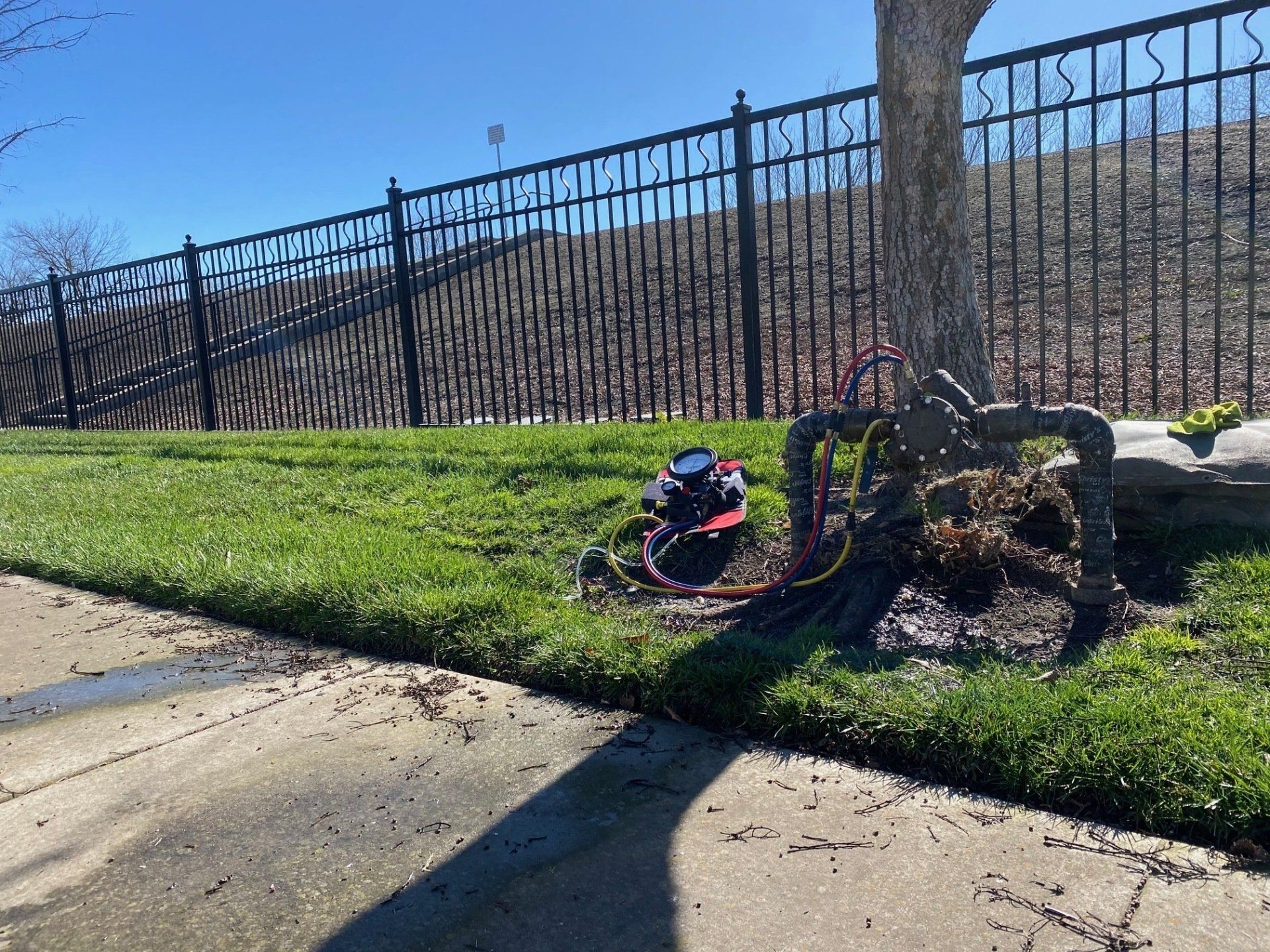 A hose is laying on the grass next to a fence.