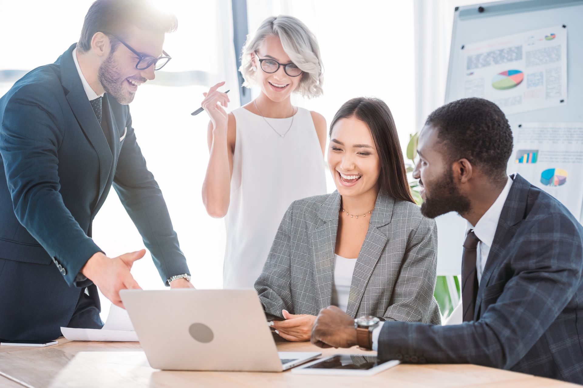 A group of business people are sitting around a table looking at a laptop computer.