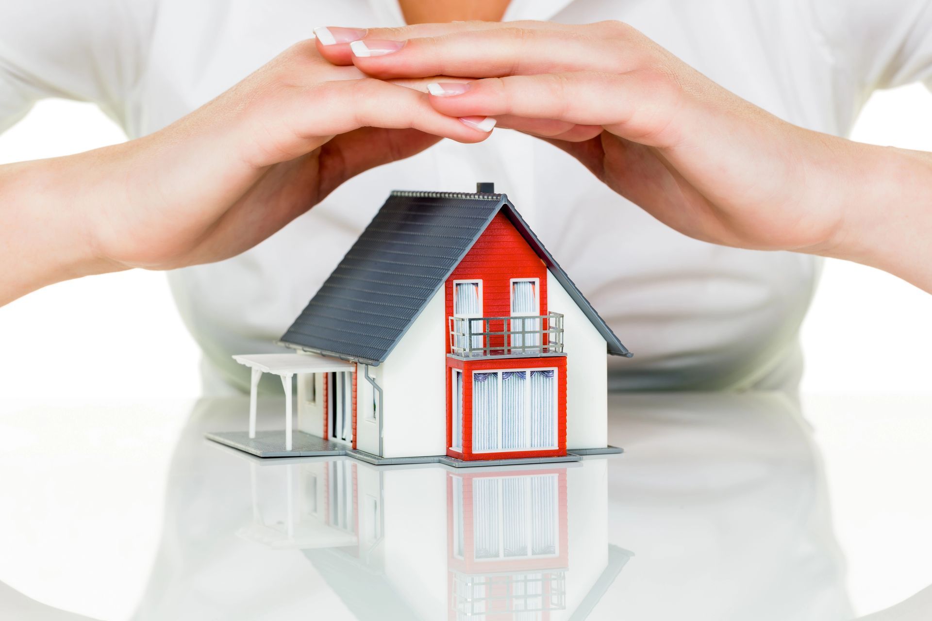 A woman is covering a model house with her hands