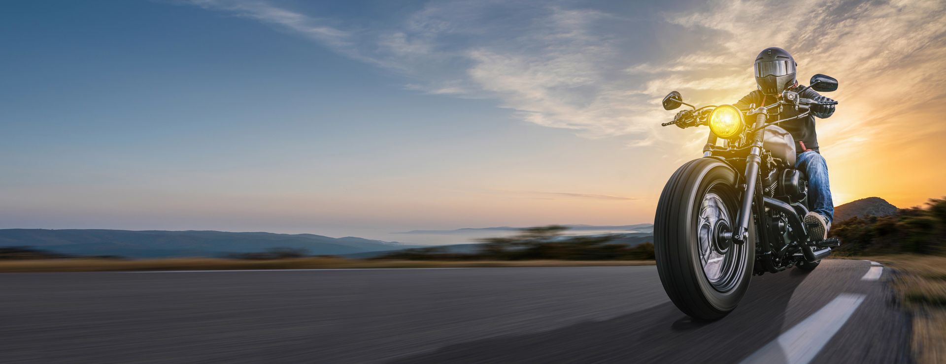 A man is riding a motorcycle down a road at sunset.