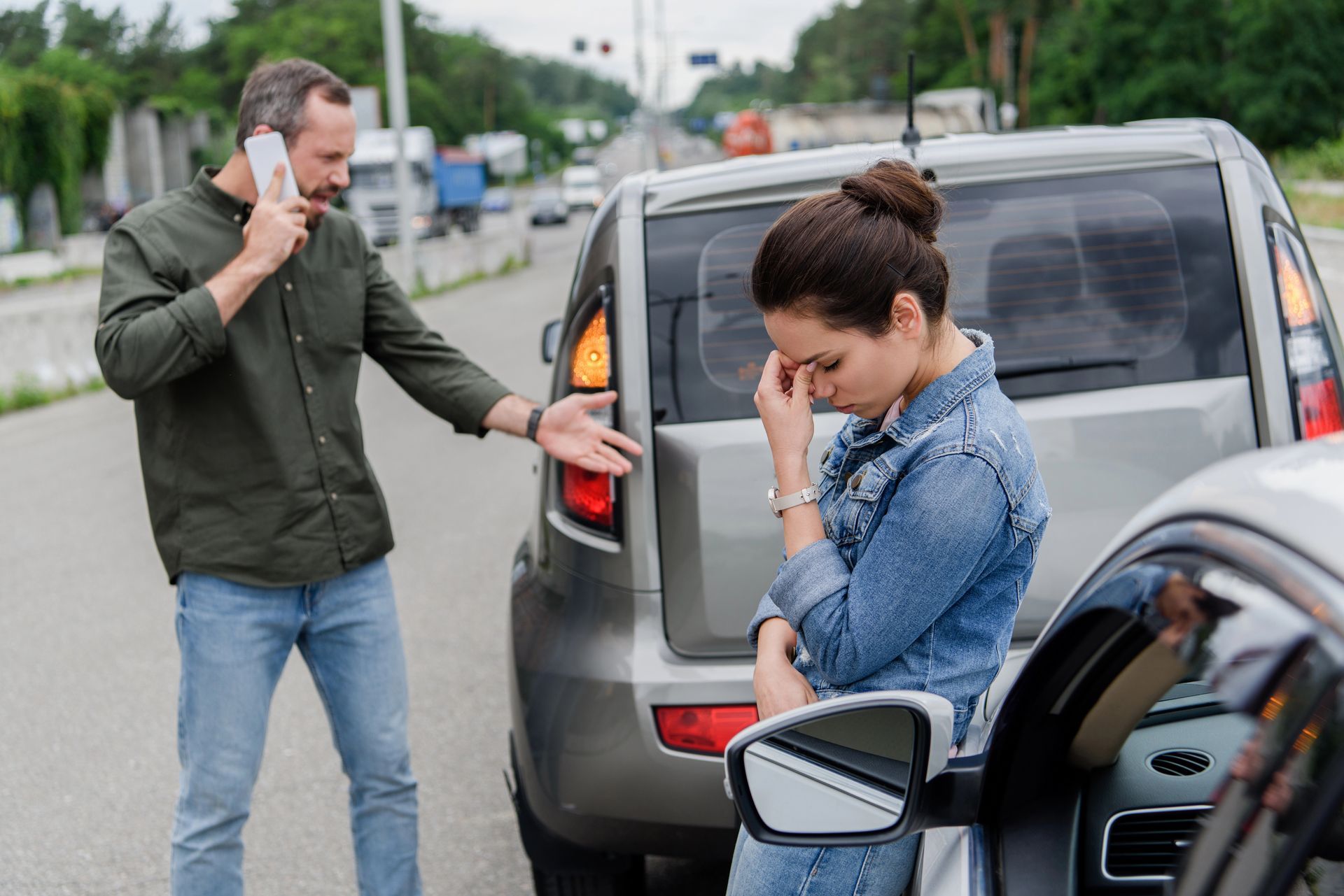A man is talking on a cell phone next to a woman sitting in a car.