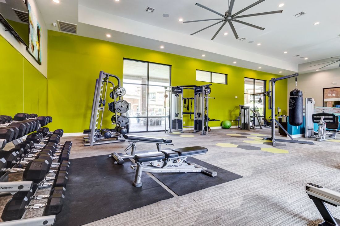 Gym with exercise equipment, dumbbells, weight machines, bright green accent wall, windows.