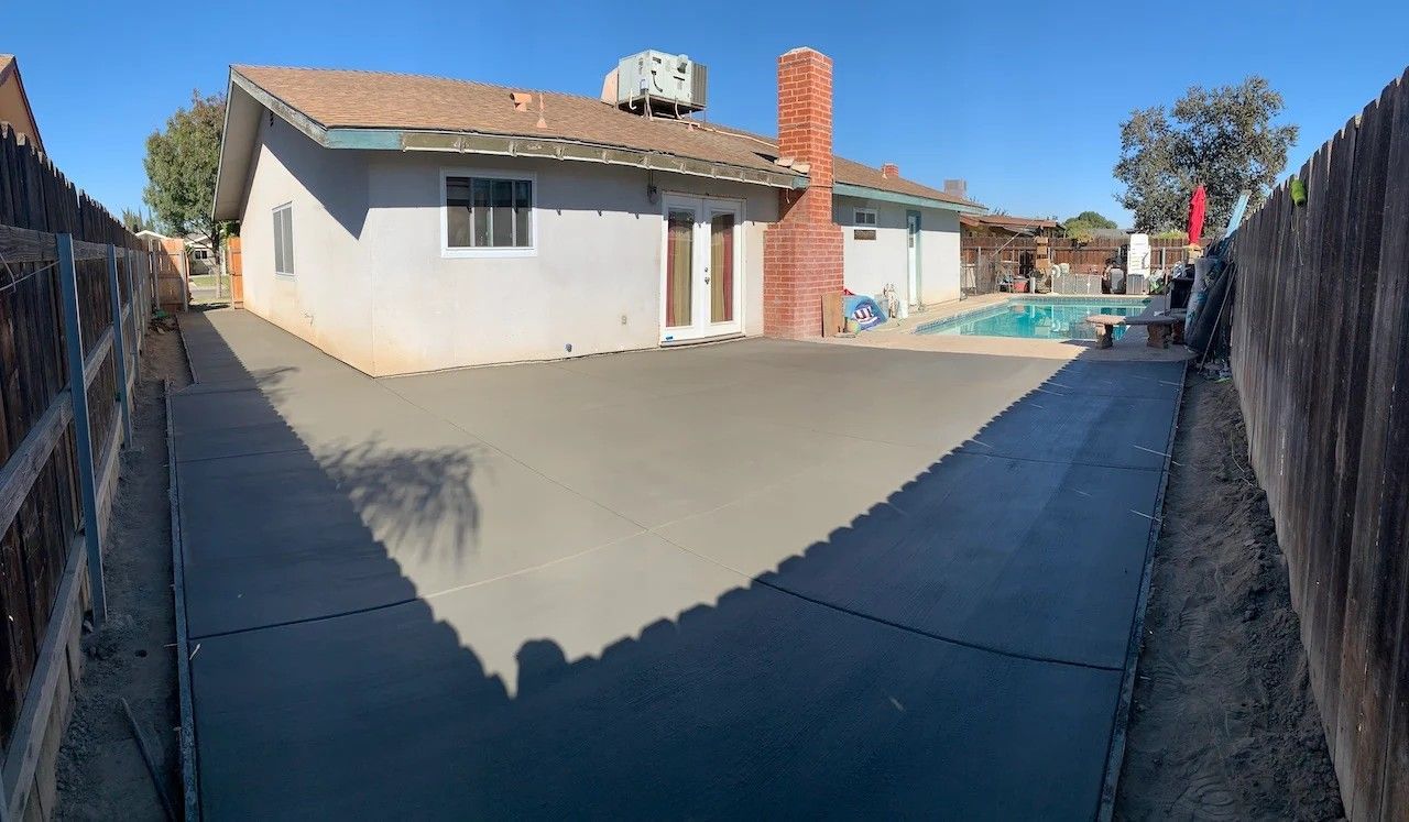 Concrete driveway leading to a single-story house with a tiled roof and fenced sides on a sunny day