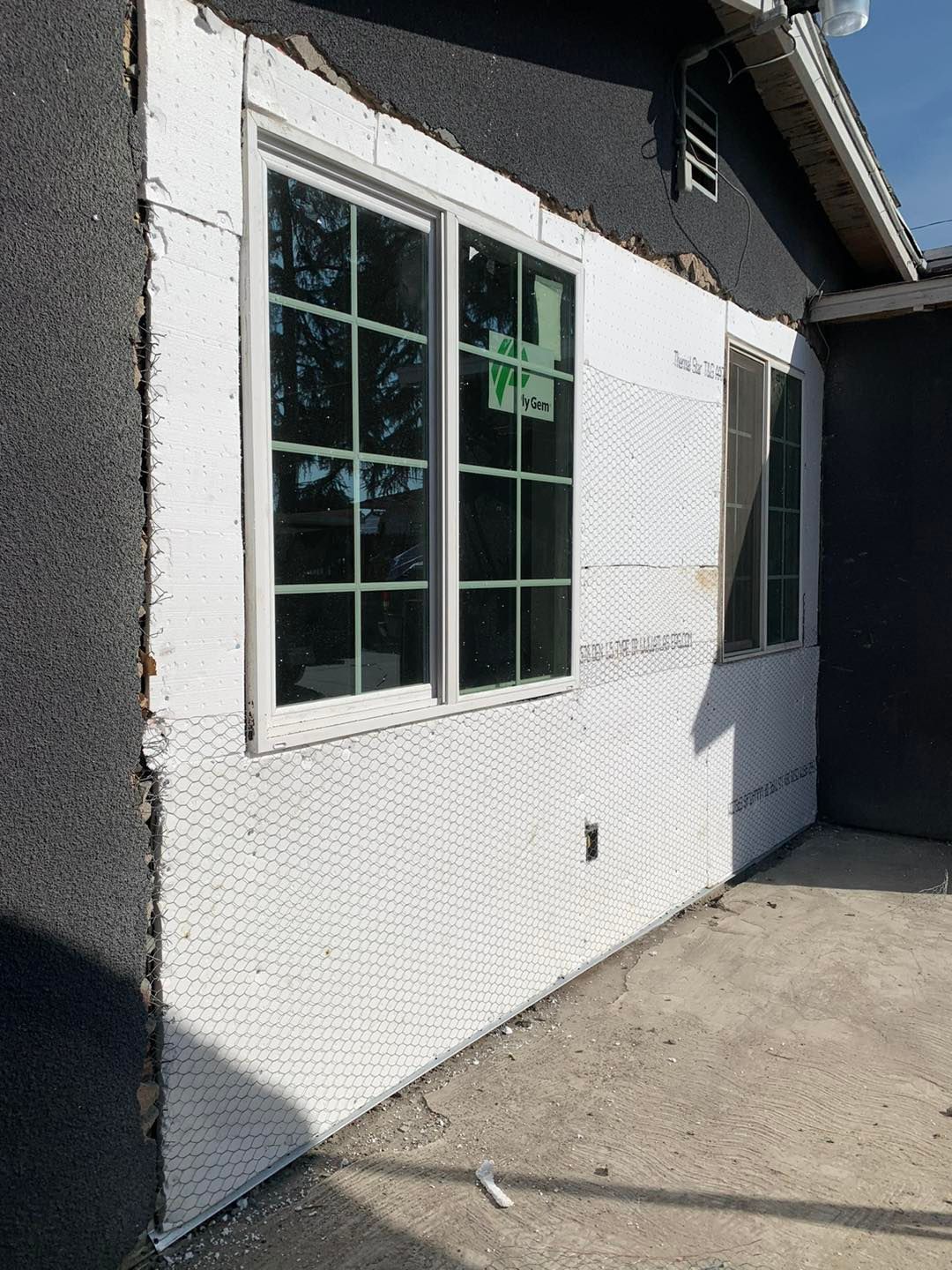 White stucco exterior wall with windows and a concrete patio in sunlight