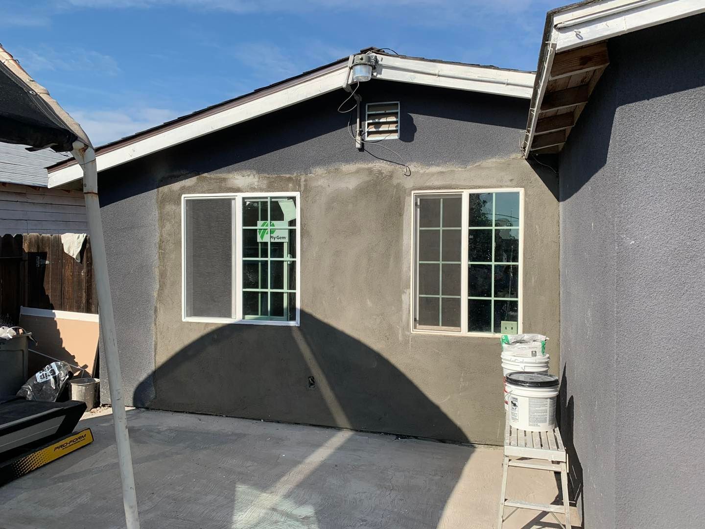 Small gray house exterior with two windows and a concrete patio under a blue sky