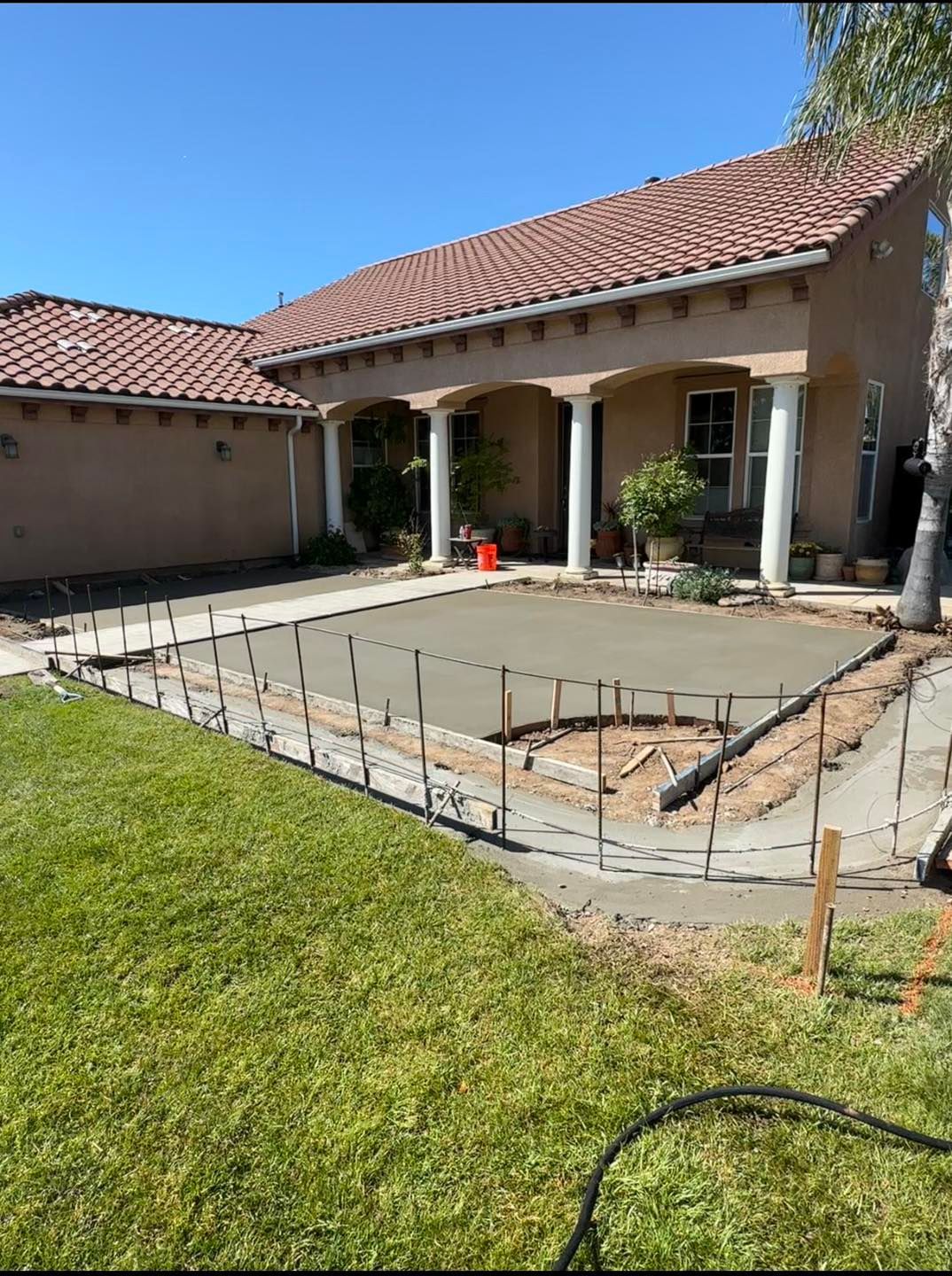 House patio under construction with rebar and freshly poured concrete beside a green lawn