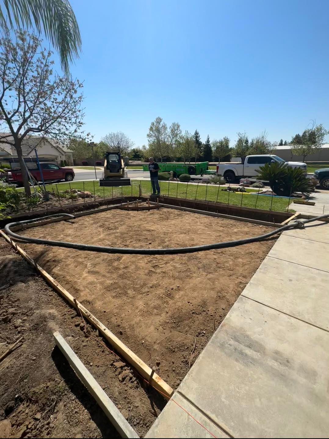 Garden bed under construction beside a sidewalk, with curved edging and bare soil on a sunny day