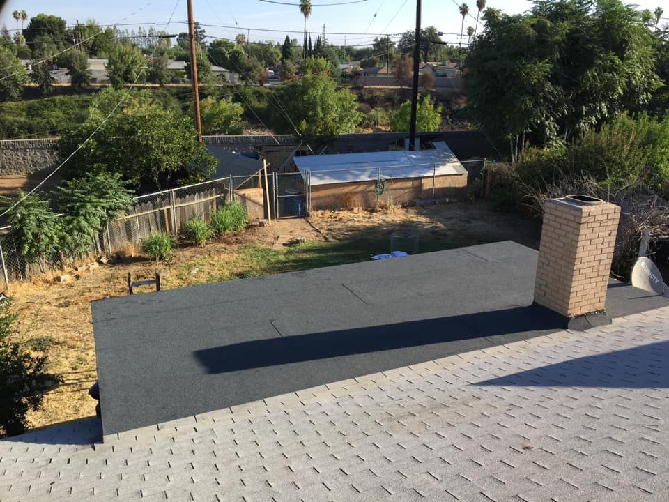 Rooftop with gray pavers, a brick chimney, and a view of trees and small buildings beyond.