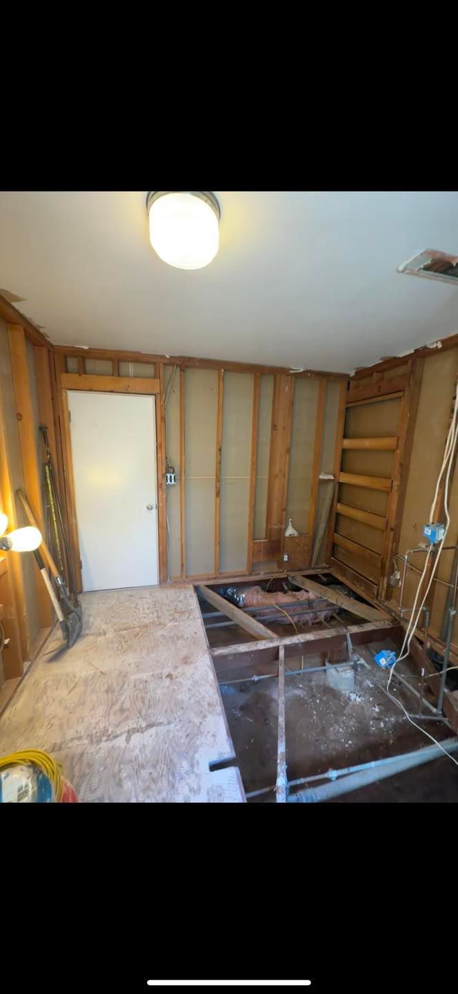 Partially renovated room with exposed wall studs, white door, carpet, and dark tiled floor section