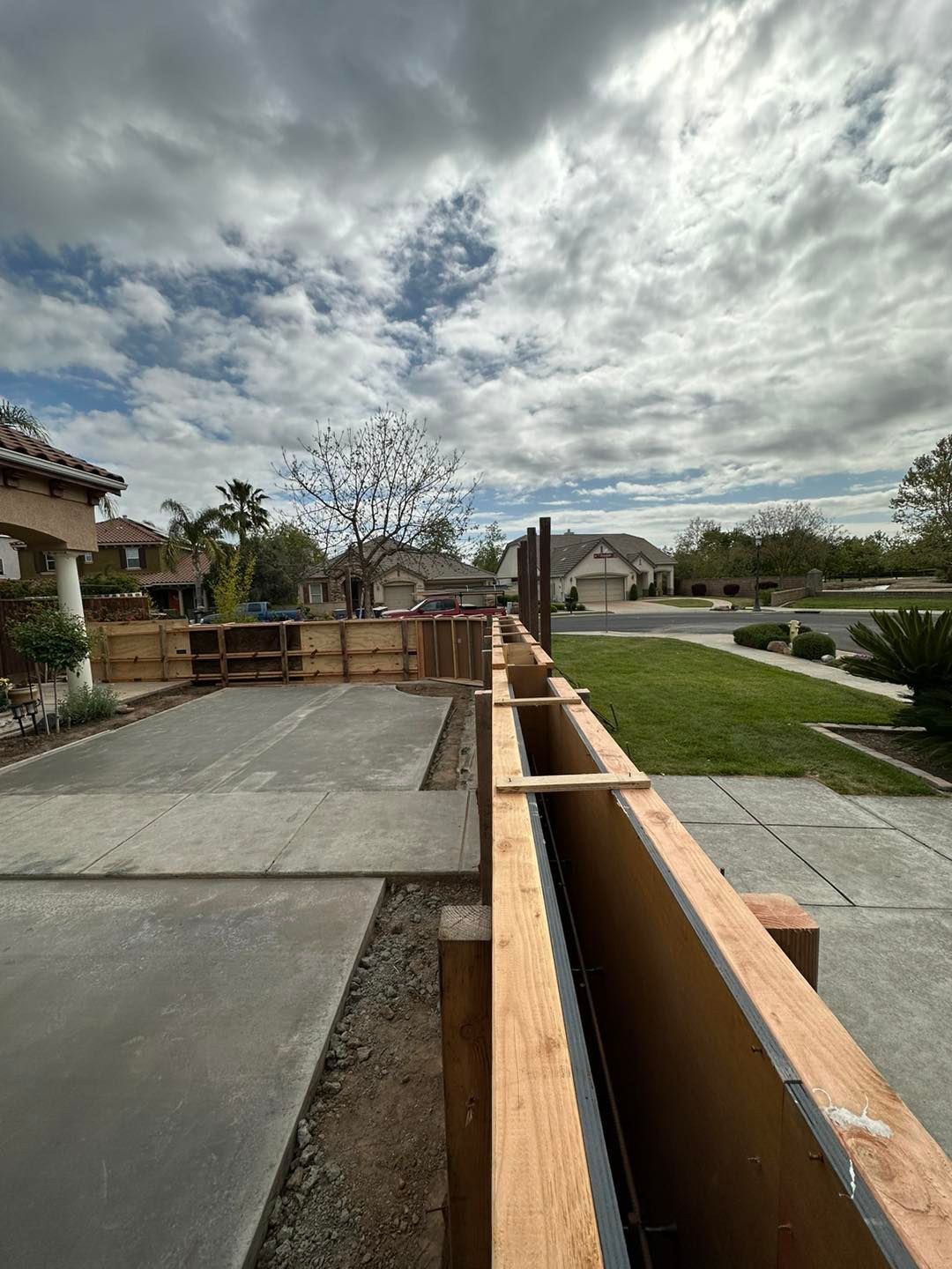 Damaged wooden railing along a concrete walkway under a cloudy sky in a suburban neighborhood