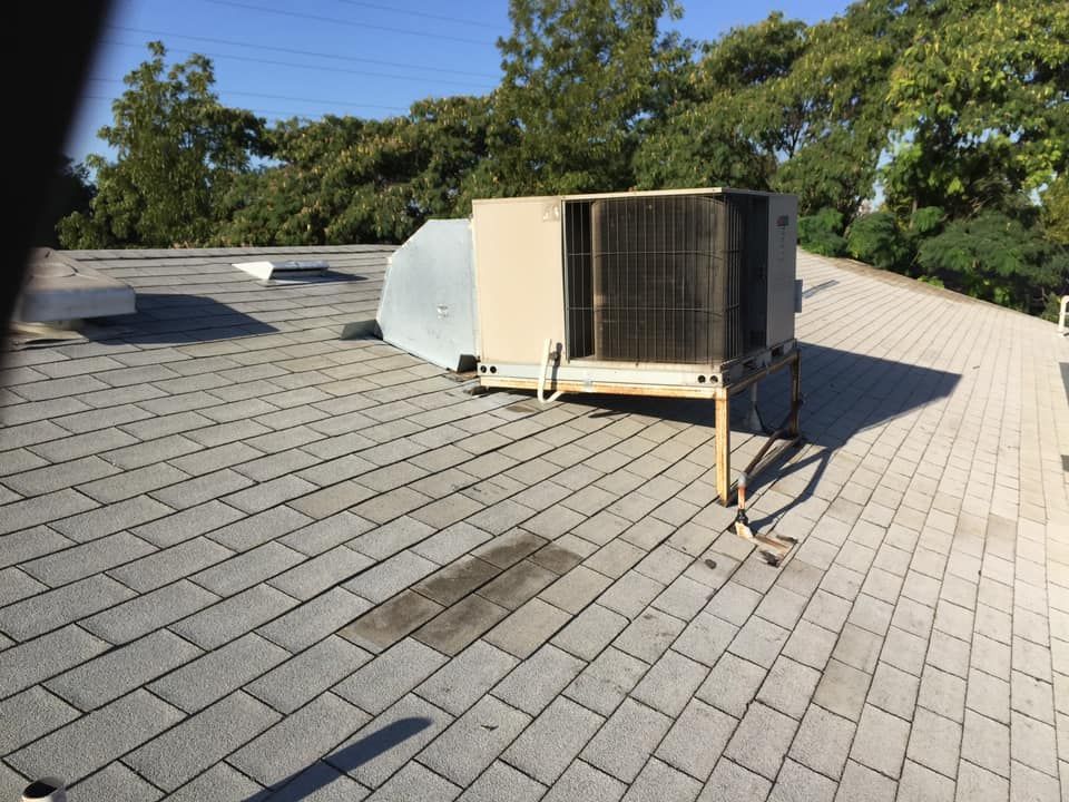 Rooftop HVAC unit on a gray shingle roof with trees and blue sky in the background