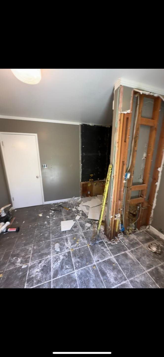 Partially demolished room with exposed framing, debris on the floor, and a gray wall beside a dark doorway