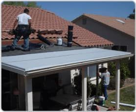 Workers installing rooftop equipment on a red-tile roof above a covered patio