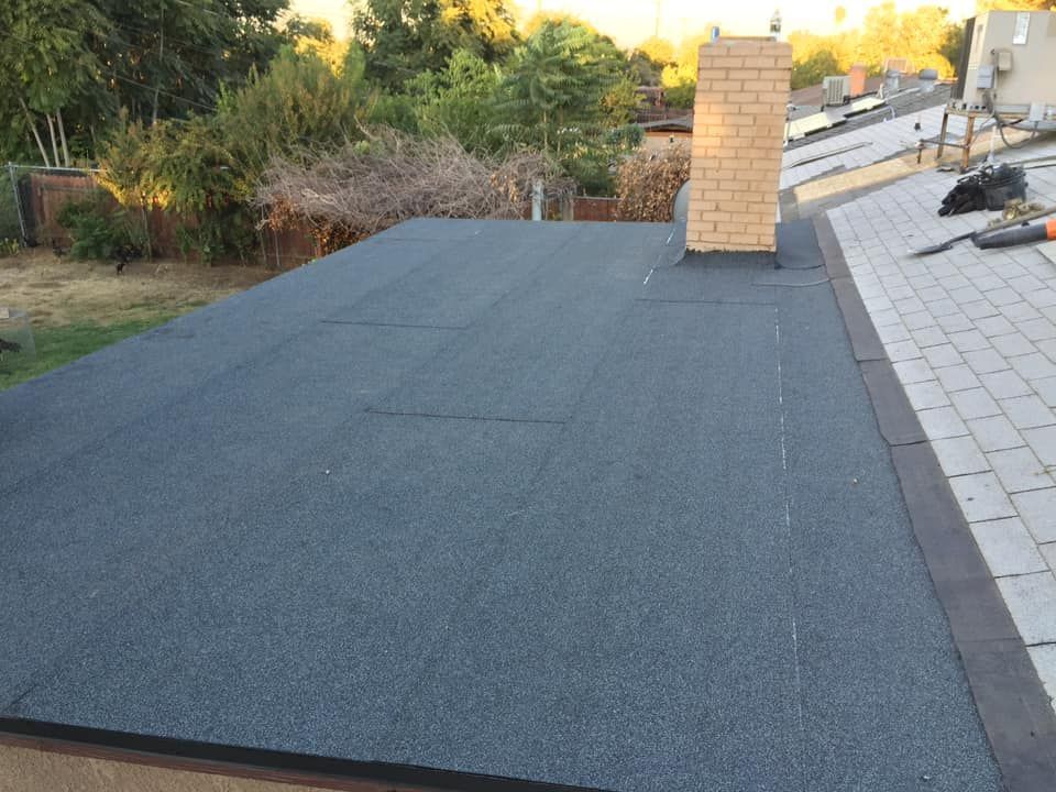 Flat rooftop with dark shingles and a brick chimney beside a paved walkway.