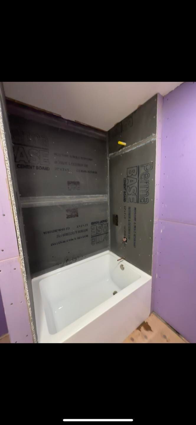 Bathroom under renovation with tiled shower surround, white tub, and gray walls