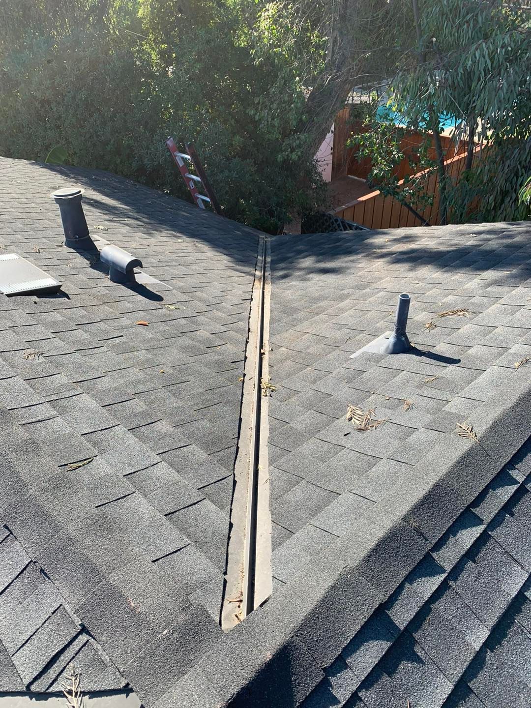 Residential roof with a long open seam between gray shingles and two vent pipes in sunlight