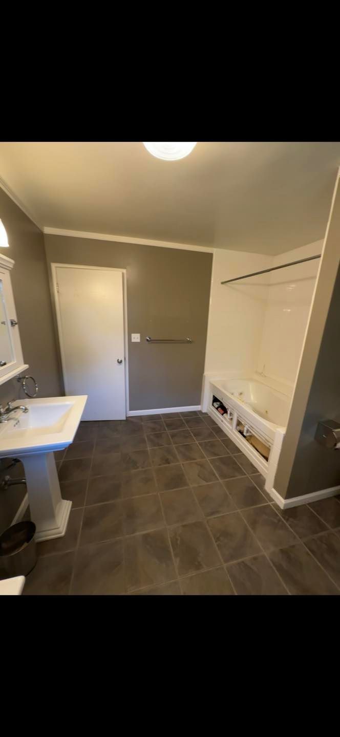 Empty laundry room with tiled floor, white walls, utility sink, and a door at the back.