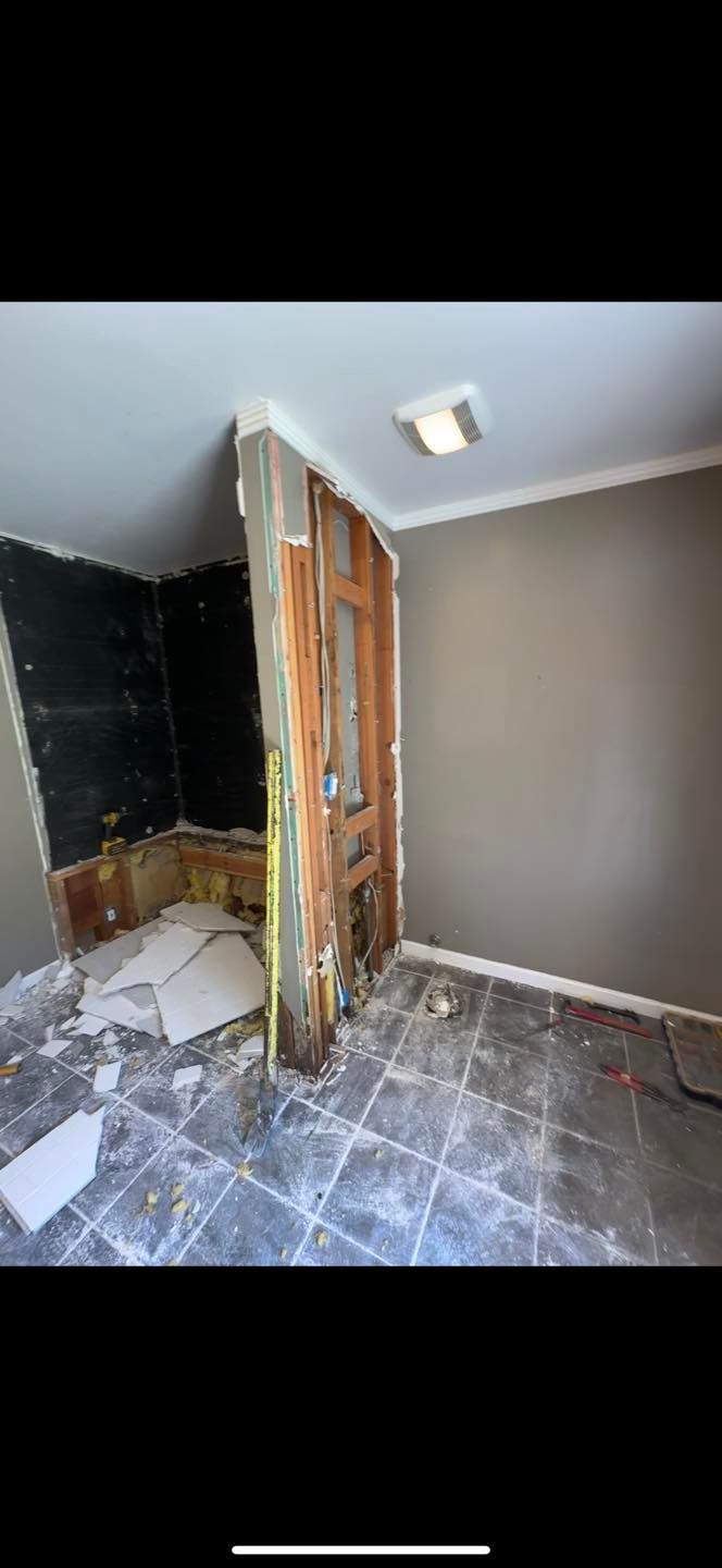 Damaged room interior with exposed wall, open door, and gray walls under a ceiling light.