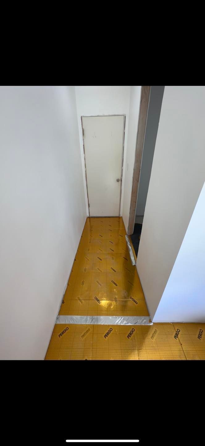 Narrow hallway with wooden floor and a white door at the end, viewed from above.