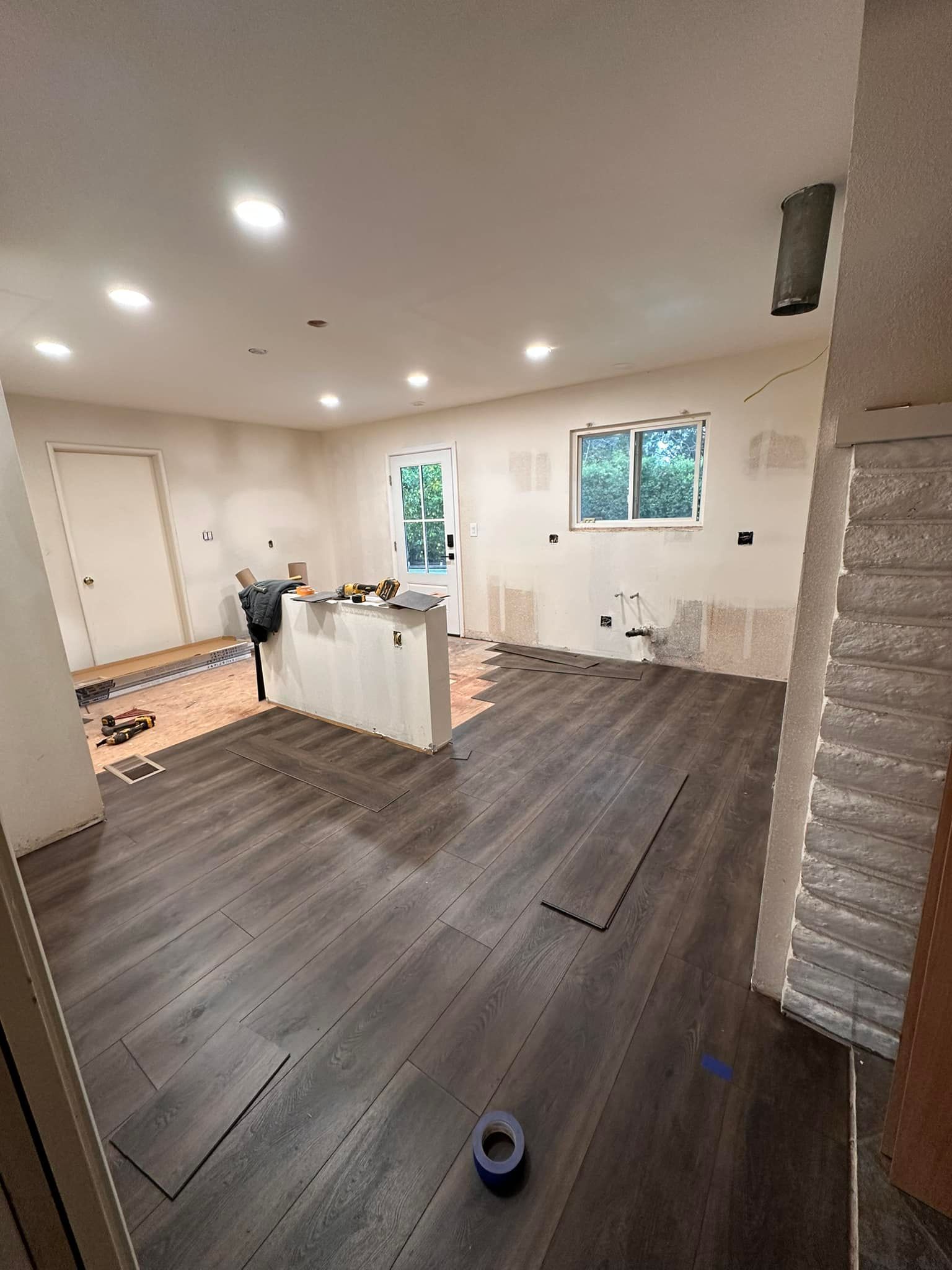 Empty modern kitchen and living area with gray wood floors, white walls, and recessed lights.
