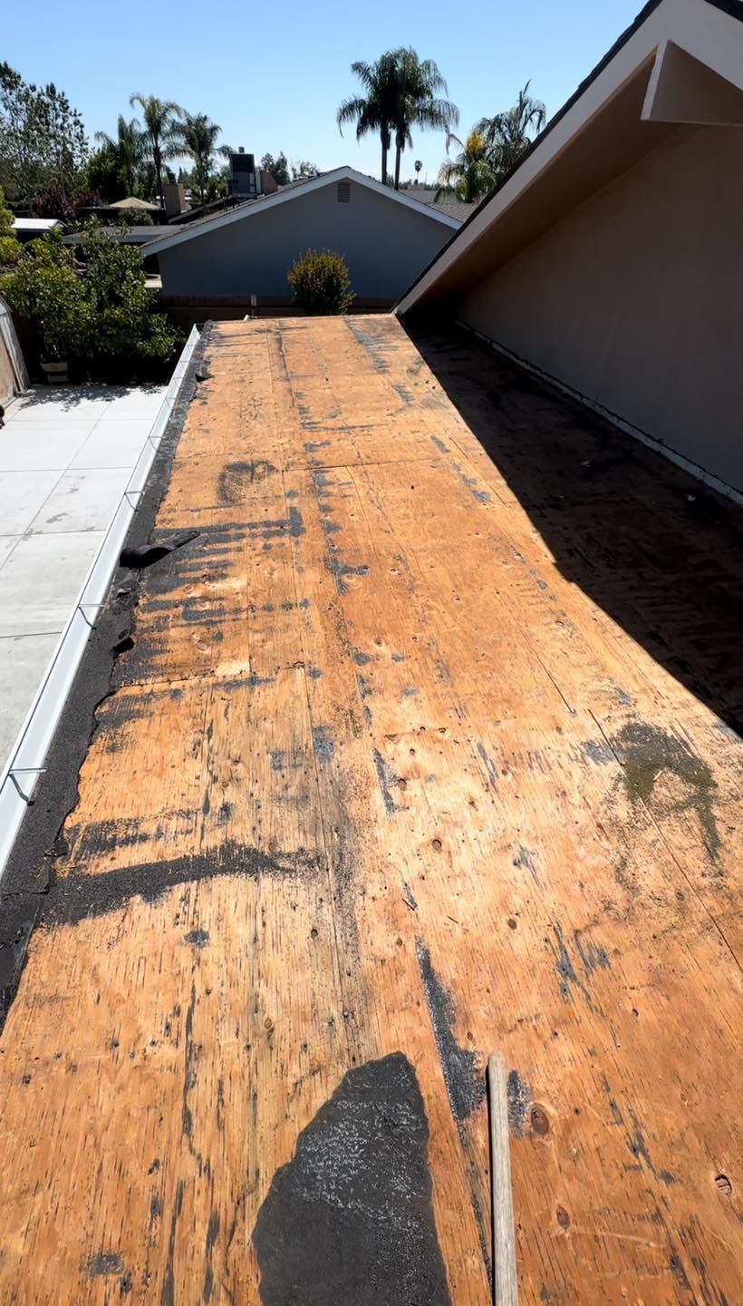 Orange plywood roof deck under construction beside a house, with palm trees in the background