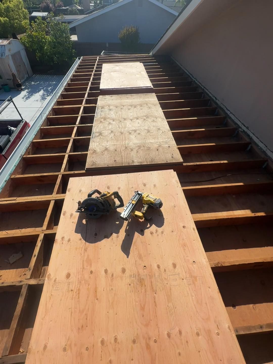 Roof deck under construction with plywood sheets, exposed joists, and tools on the foreground panel.