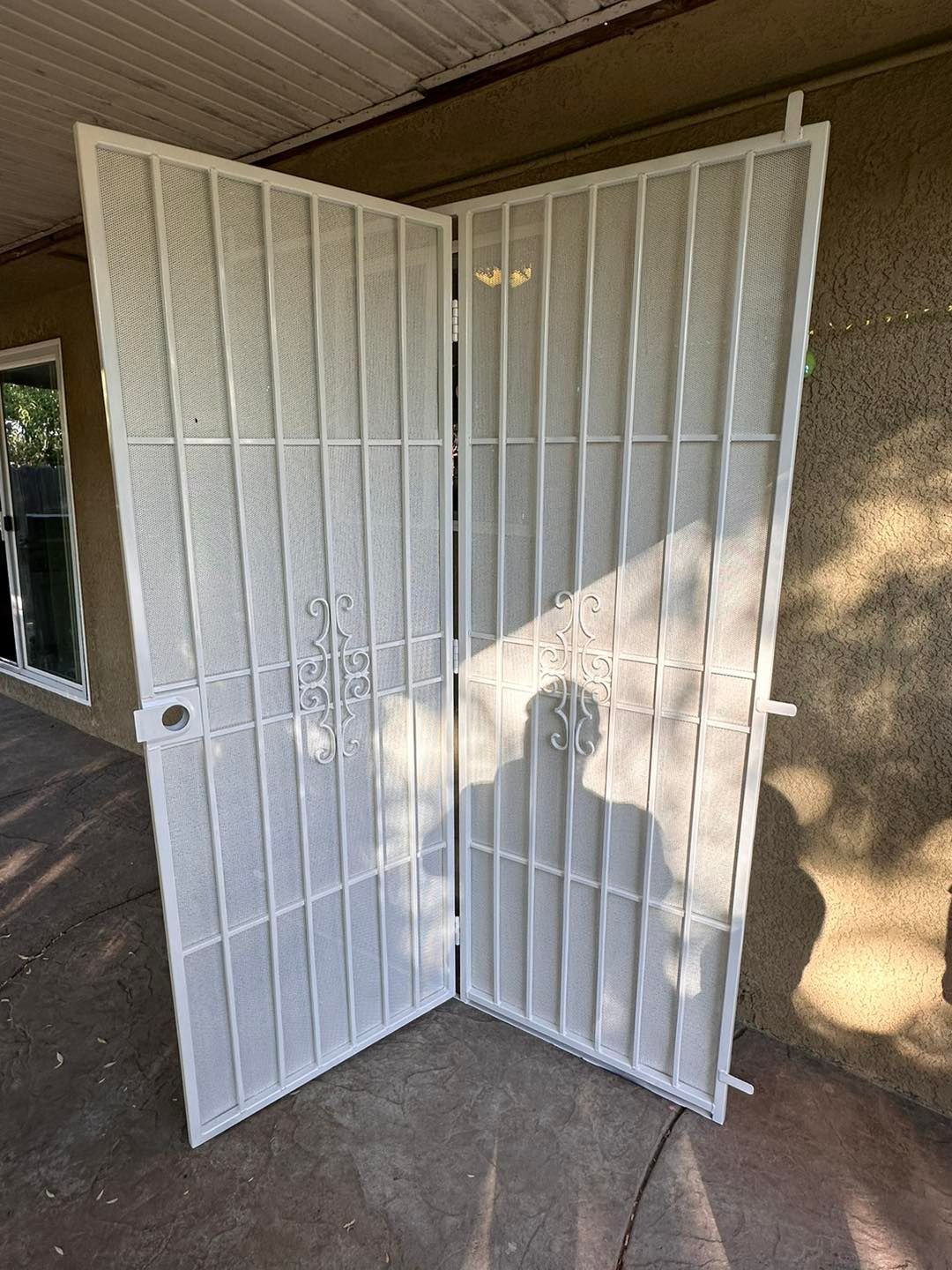 White metal security gate propped open on a porch, with sunlight and shadows on the wall.