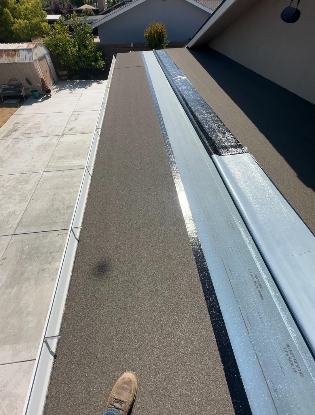 Rooftop walkway with gravel and metal flashing beside a building, viewed from above.