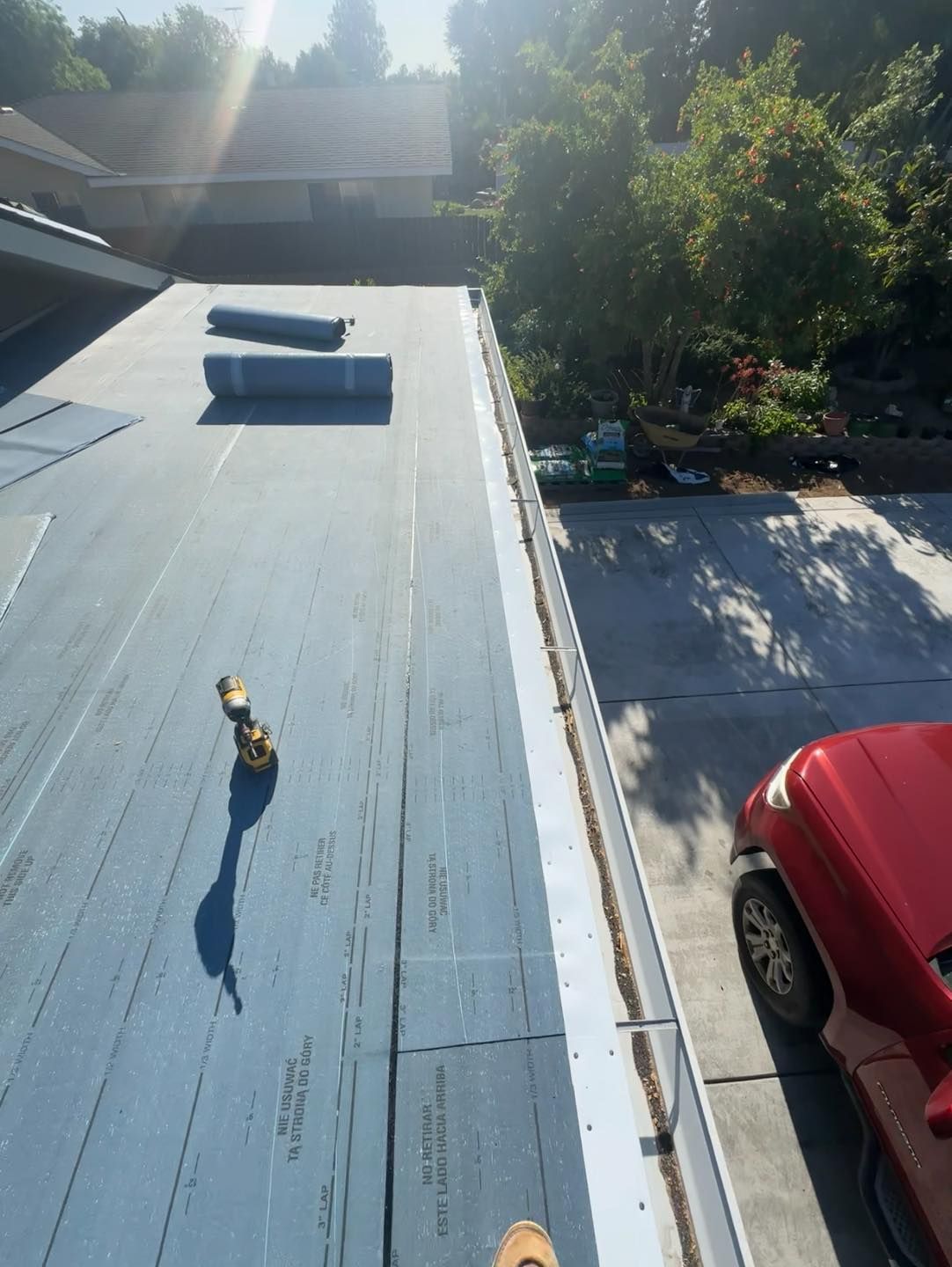 Rooftop with blue surface, vents, trees below, and a red car parked beside the building.