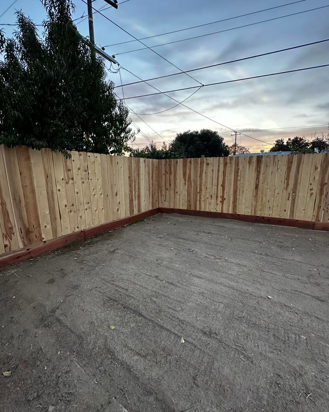 Empty fenced backyard corner with a concrete pad, wooden privacy fence, and dusk sky overhead