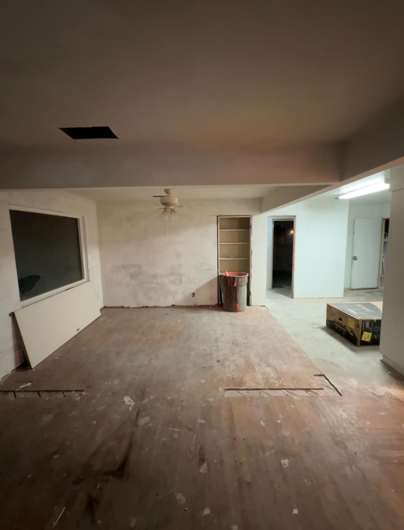 Empty, partially renovated room with bare floor, white walls, and exposed patchwork ceiling.