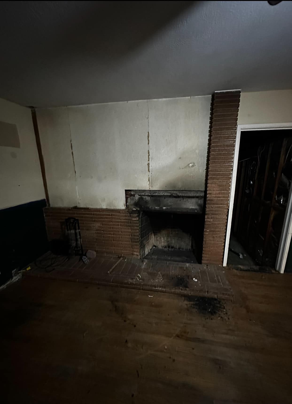 Dim room with a brick fireplace, wooden floor, and open doorway to the right.