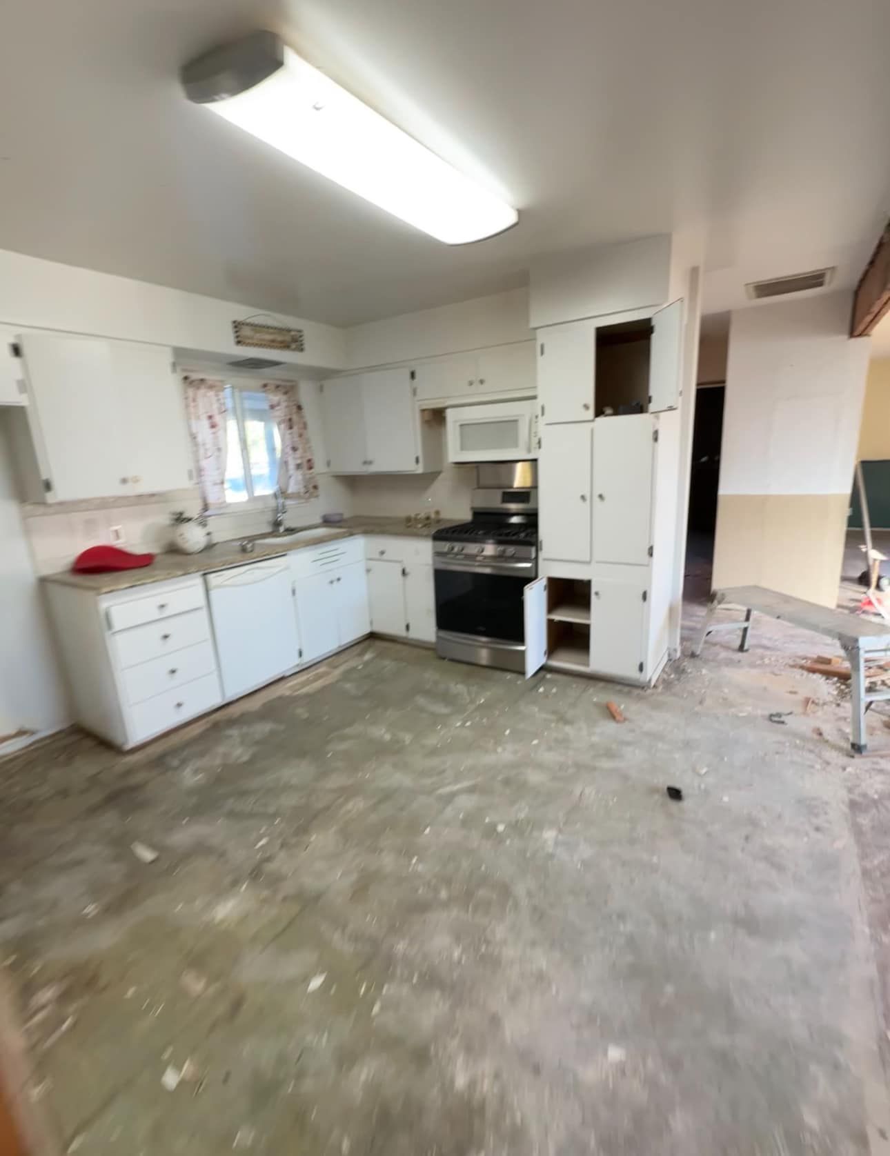 Empty kitchen with white cabinets, black stove, and bare concrete floor under fluorescent light