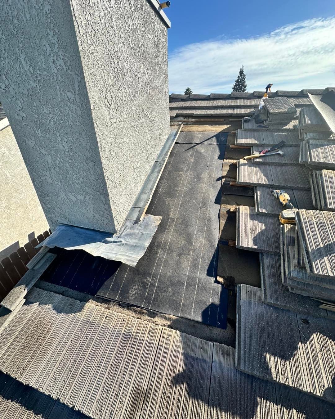 Rooftop with black waterproof membrane, HVAC equipment, and a tall wall under a blue sky
