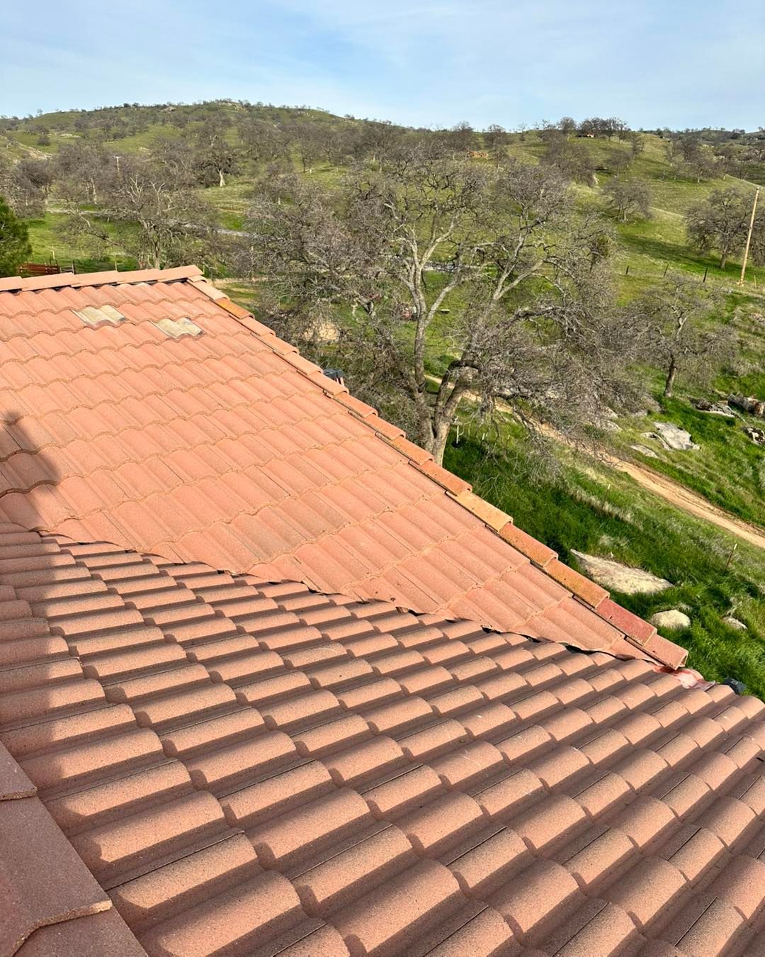 Terracotta roof overlooking a green hillside and dirt path under a clear sky