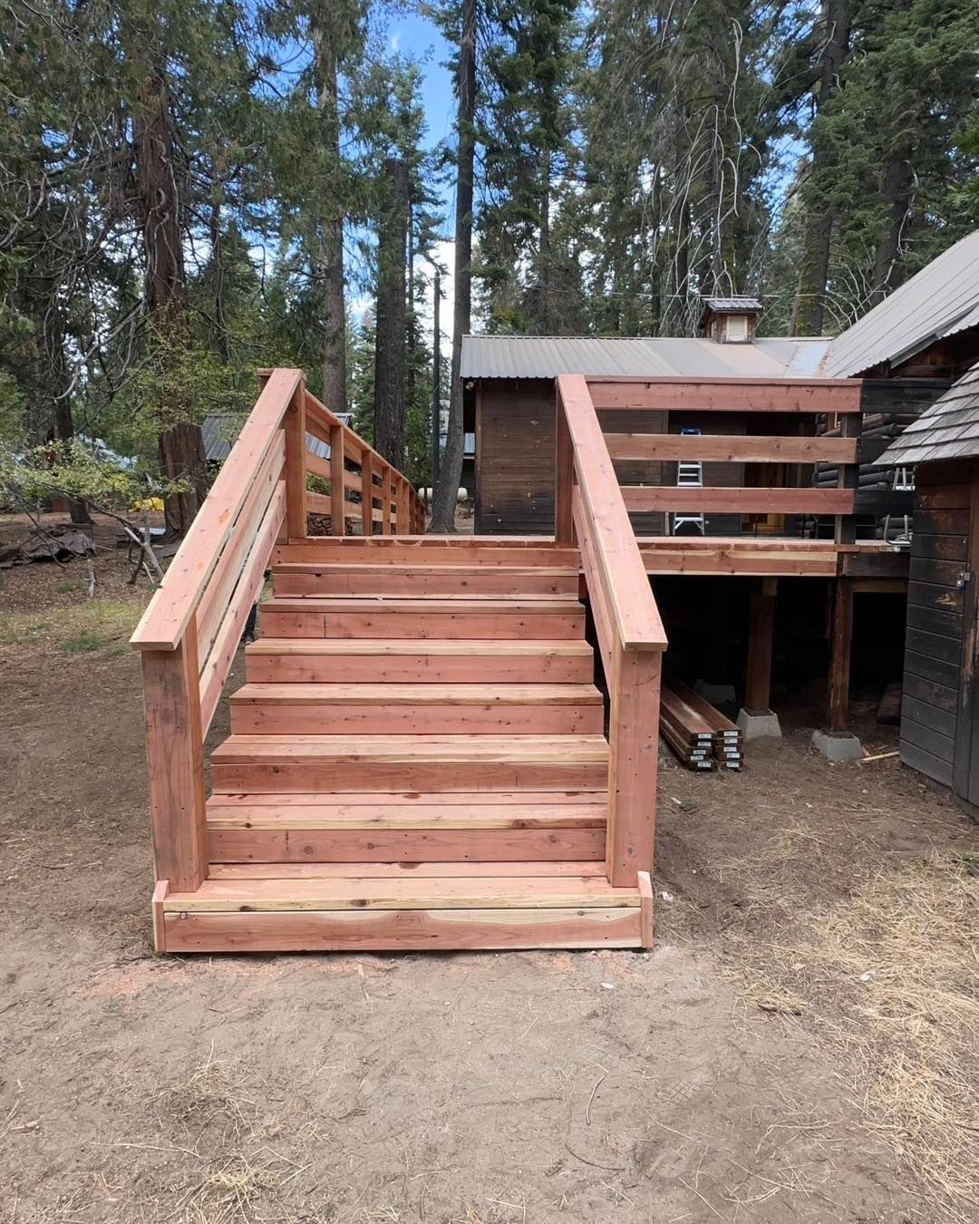 Wooden staircase with railings leading up to a cabin deck in a wooded yard
