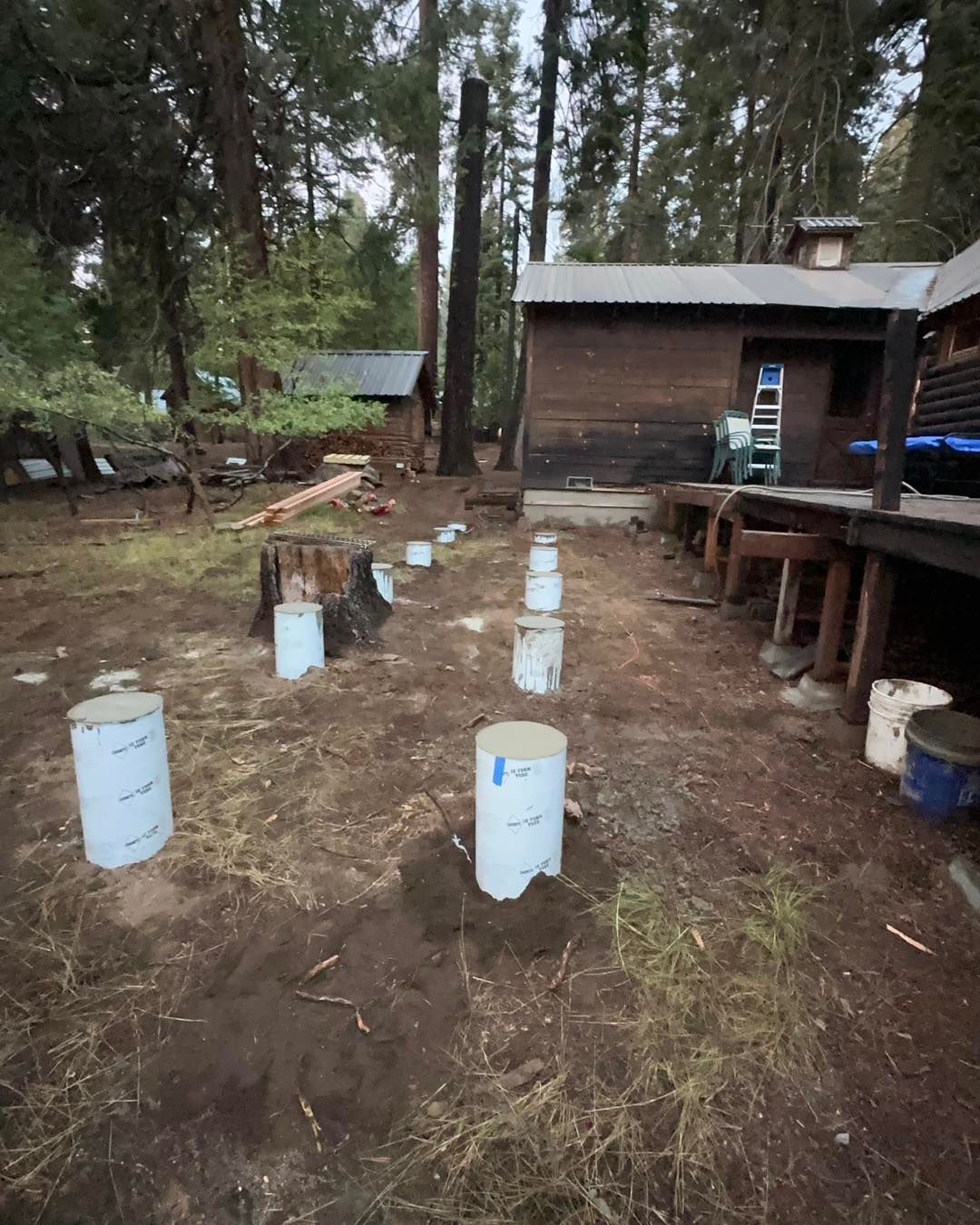 Buckets arranged in a forest clearing beside a wooden cabin and deck with trees in the background