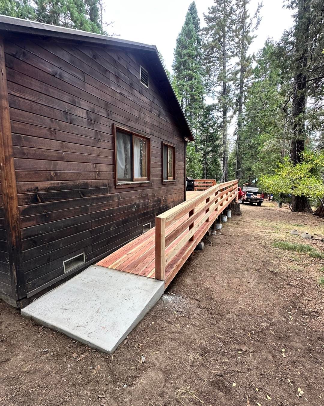 Wooden cabin with an accessible ramp and railing in a forested yard.