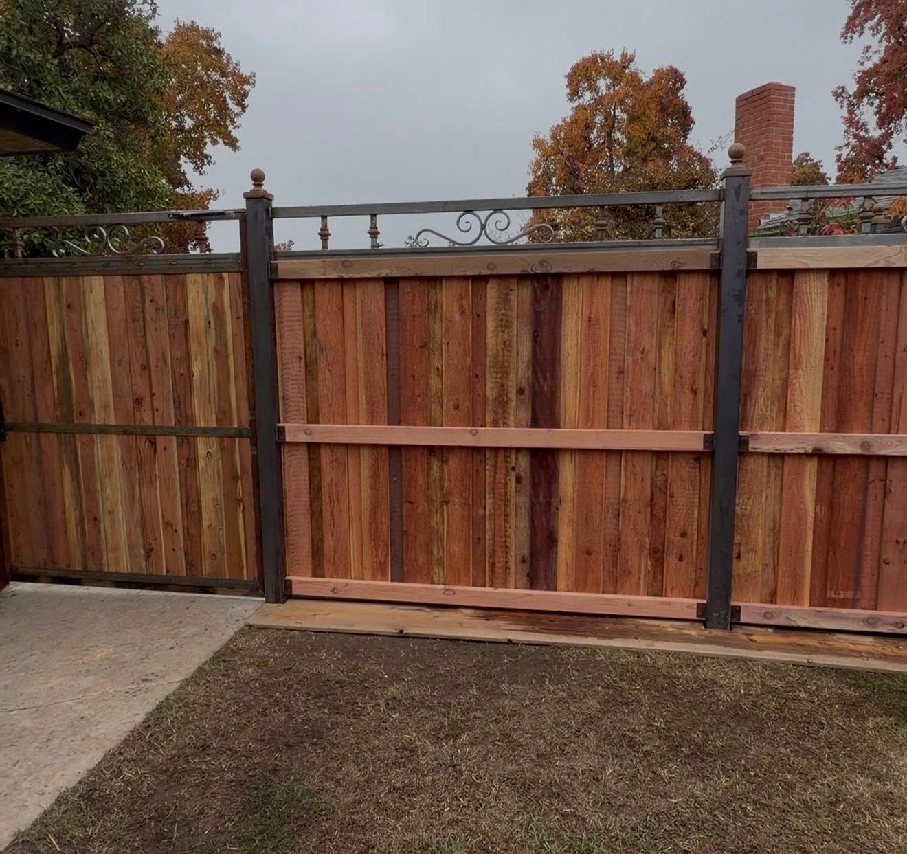 Wooden privacy fence with dark metal posts and decorative top rail beside a concrete driveway and lawn.