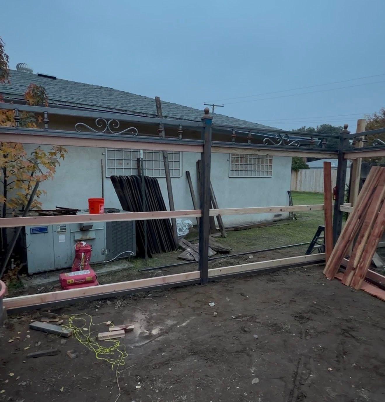 Backyard with a white shed, stacked lumber, and a metal frame in a muddy work area