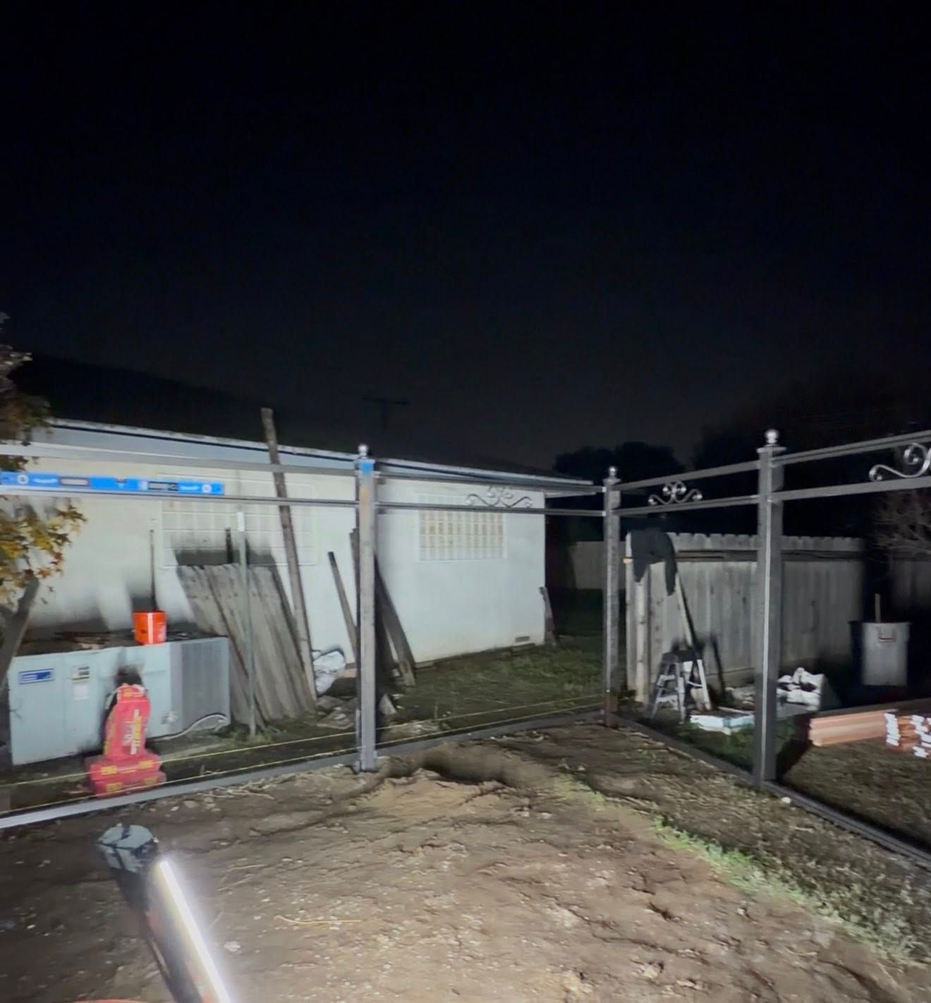 Nighttime backyard with a fenced patio, concrete ground, tools, and a white shed under dark sky
